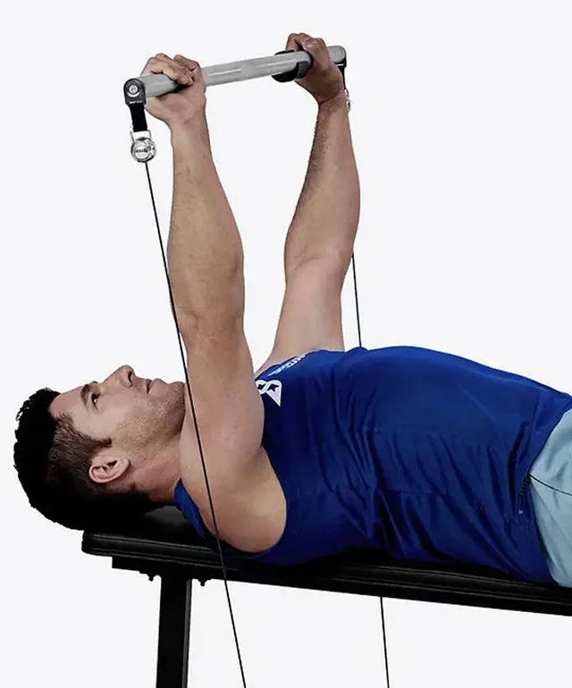A man lying on a bench pressing a bar attached to cables